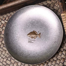 Load image into Gallery viewer, Rhodeus Plate from above on a woven mat, showing the brass bitterling and antiqued stainless steel finish